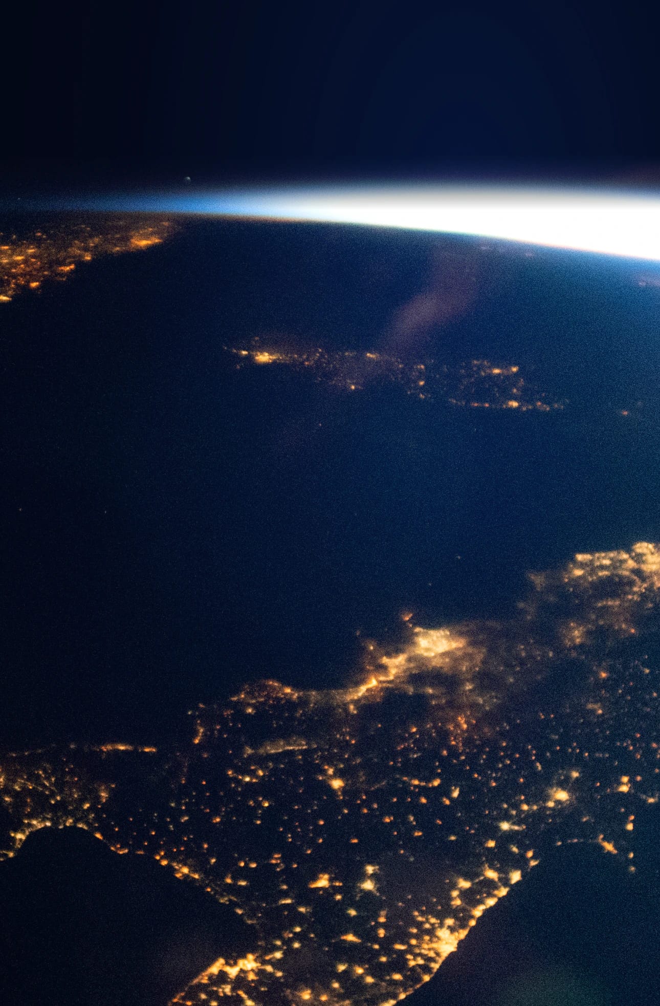 Southern Italy at night with sunrise breaking over the horizon, photographed from the International Space Station